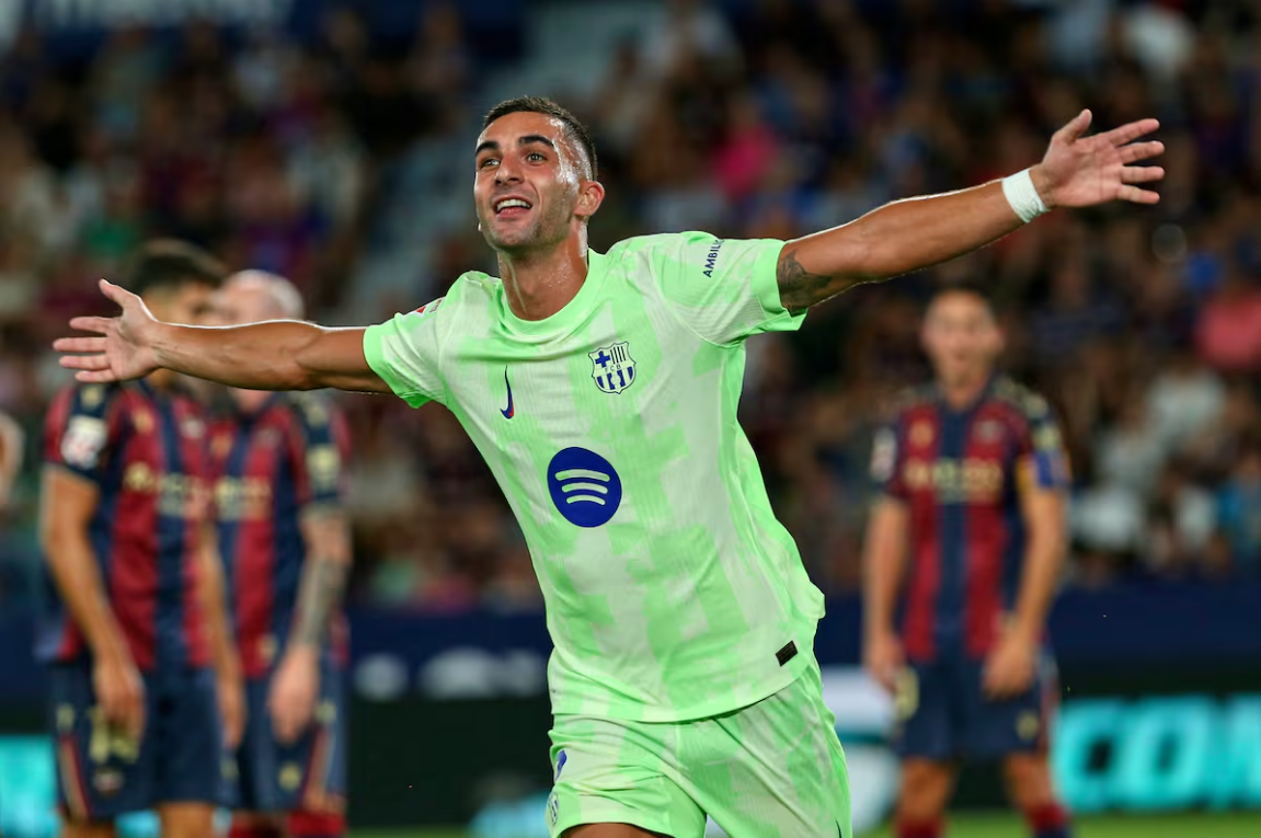 Soccer player in a bright green FC Barcelona kit celebrating with arms wide open during a match, with opponents in red and blue jerseys blurred in the background.